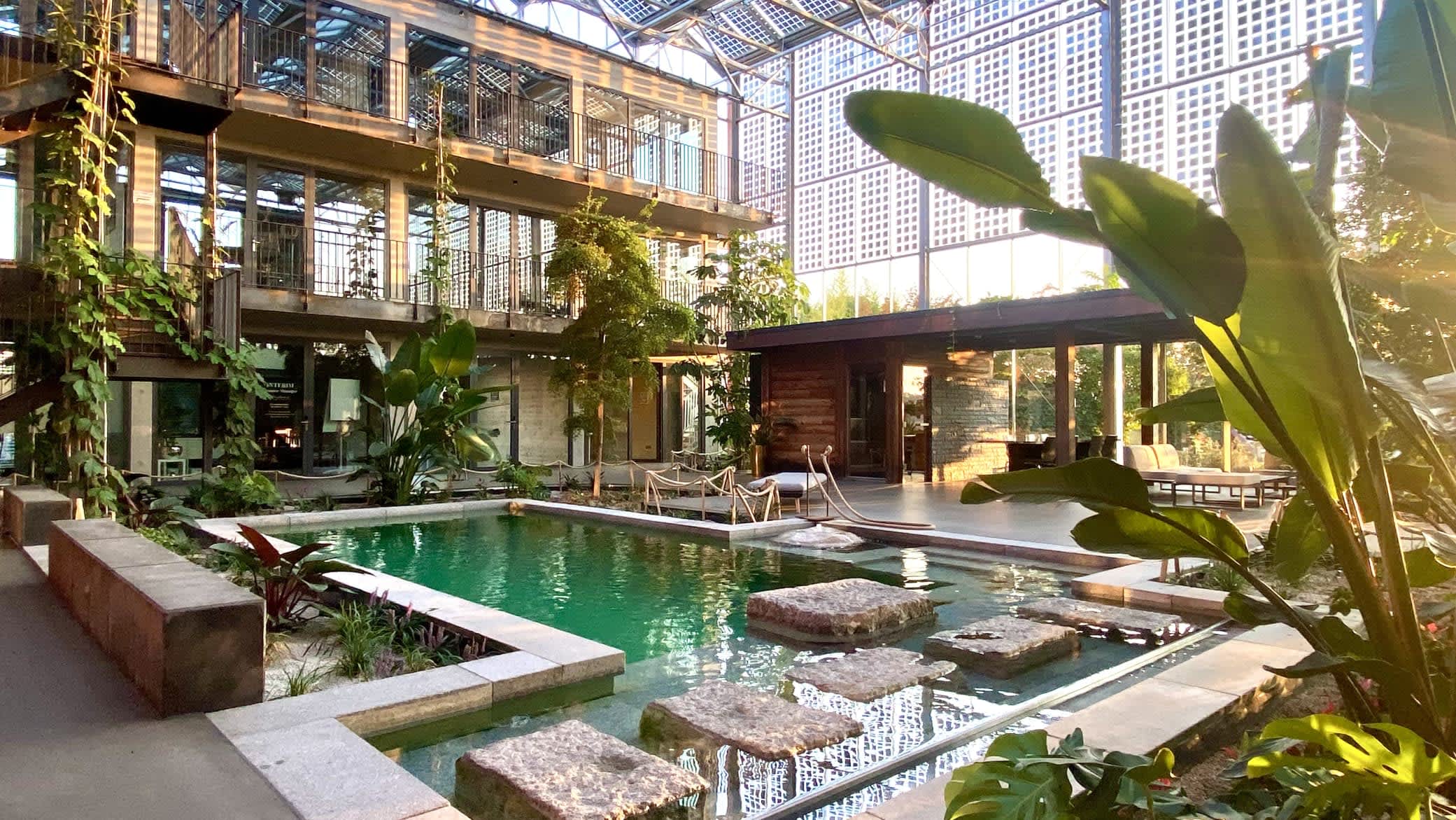 Lichtdurchflutetes Gewächshaus mit Wasserbecken und tropischen Pflanzen